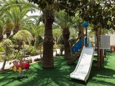 Ein Kinderspielplatz mit Rutschen, Schaukeln und einem weichen Bodenbelag aus grünem Kunststoff.