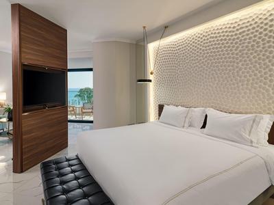 Modernes Hotelzimmer mit großem Bett, strukturierter Wand und Blick auf die Terrasse.