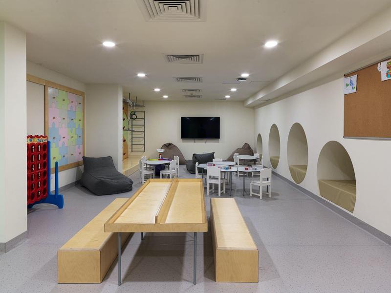 Heller, moderner Raum mit Holzbank, Sitzsäcken, Tischen, Fernseher und Ablagefächern in weißem Design.