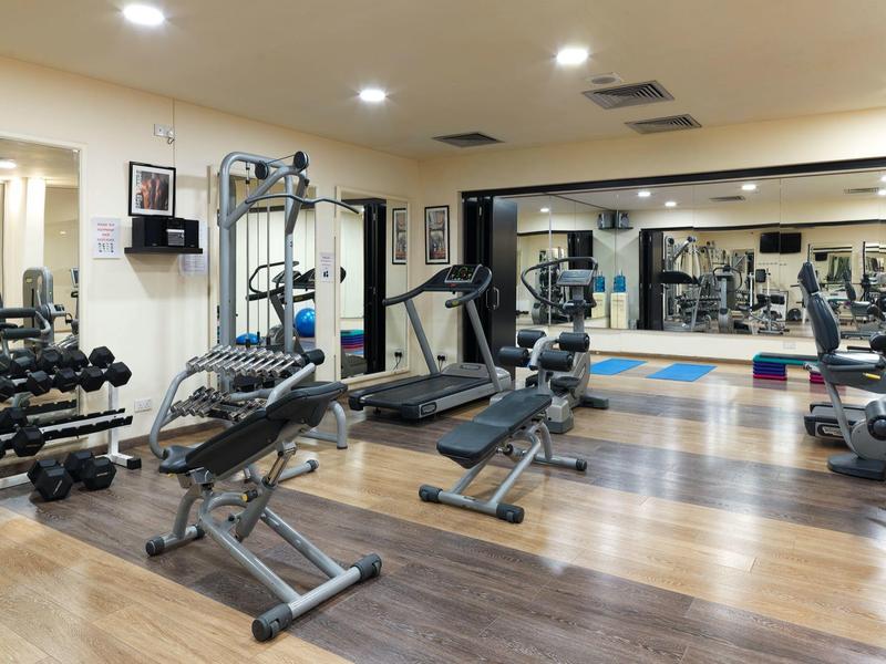 Moderner Fitnessraum mit Hanteln, Trainingsgeräten und großen Spiegeln an den Wänden.