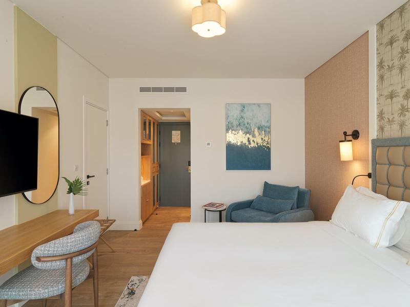 Modernes Hotelzimmer mit großem Bett, Schreibtisch, Stuhl, Sofa und neutralen Farben.
