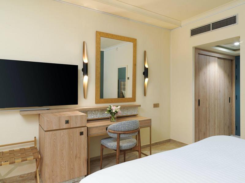 Modernes Schlafzimmer mit Flachbildfernseher, Holzschreibtisch, Stuhl, Spiegel und Bett im Vordergrund.