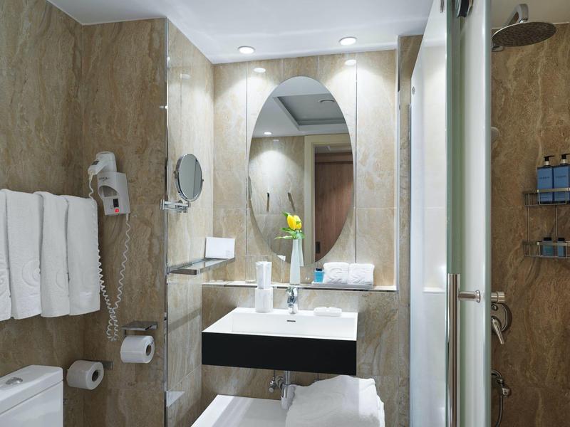 Kleines, modernes Badezimmer mit ovalem Spiegel, weißem Waschbecken und braunen Fliesen.