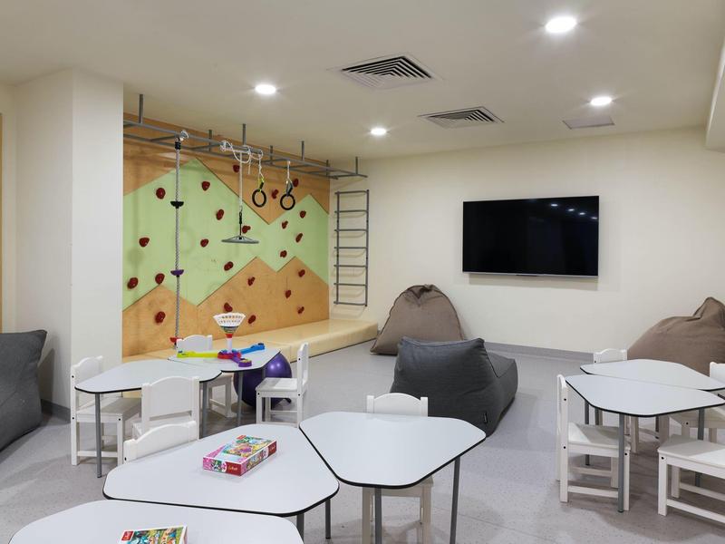 Moderner Spielraum mit Kletterwand, Sitzsäcken, Tischen und Stühlen in hell gestaltetem Zimmer.