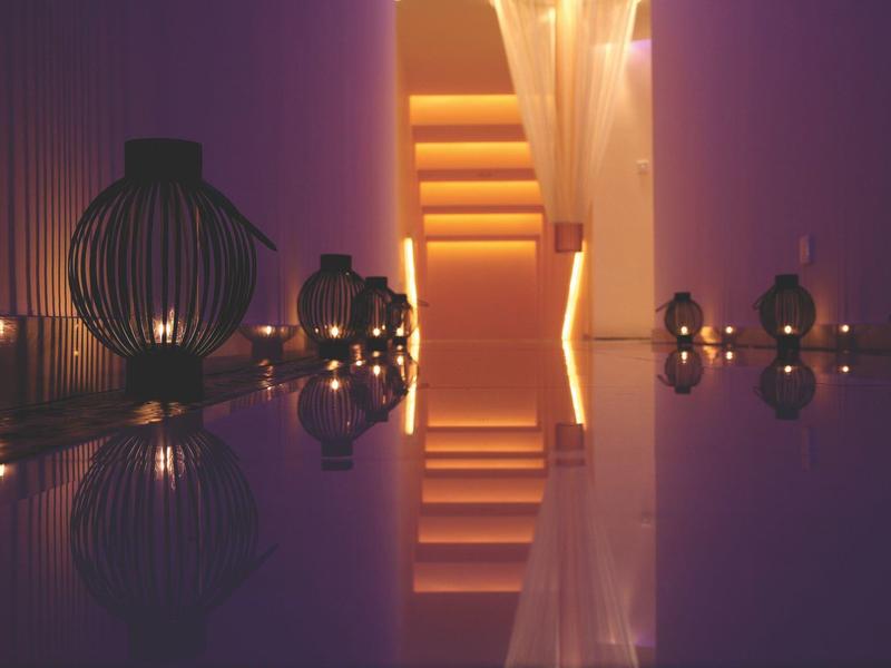 Dimmer Raum mit warmem Licht, Kerzen und dekorativen Laternen, reflektiert auf glänzendem Boden.