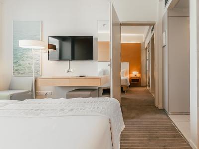 Moderní hotelový pokoj s pohodlnou postelí, televizí s plochou obrazovkou a chodbou vedoucí do dalšího pokoje.