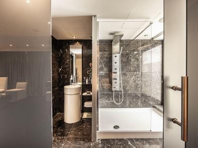 Moderní koupelna se skleněnou sprchou, umyvadlem a mramorovými dlaždicemi v hotelovém pokoji.