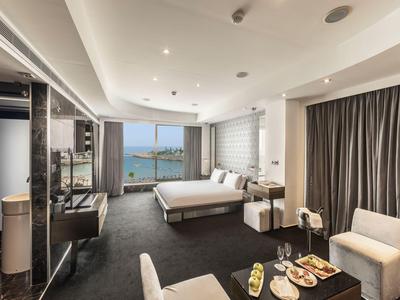 Moderní hotelový pokoj s výhledem na moře, dvěma postelemi a posezením s občerstvením.