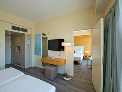 Nowoczesny pokój hotelowy z dwoma łóżkami, telewizorem, biurkiem i widokiem na sąsiedni pokój.