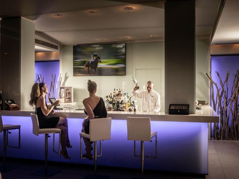 Moderne Bar mit leuchtender Theke, zwei Frauen und Barkeeper in stilvoller, gedämpfter Beleuchtung.