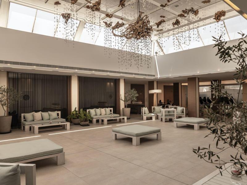 Großer heller Raum mit modernen weißen Möbeln, Pflanzen und großen Fenstern im Oberlichtbereich.