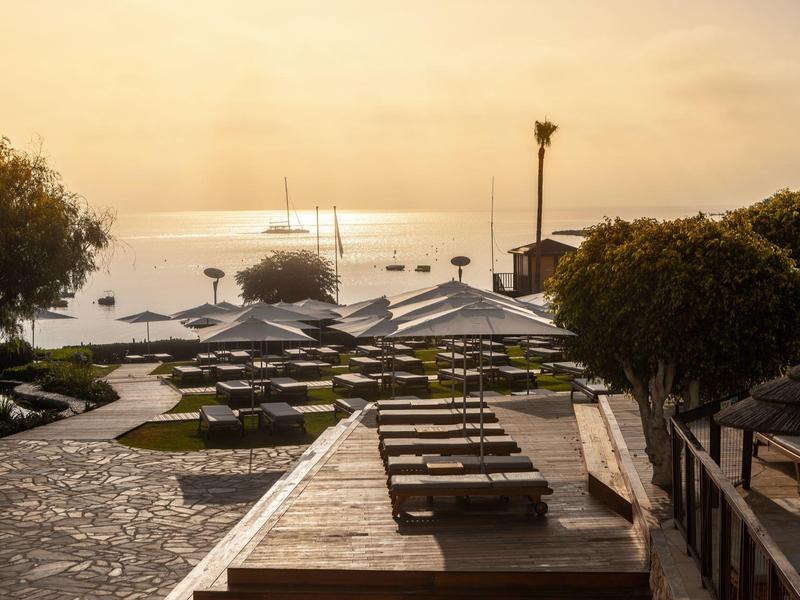 Strand mit Liegestühlen, Sonnenschirmen und Blick auf ruhiges Meer im warmen Abendlicht.