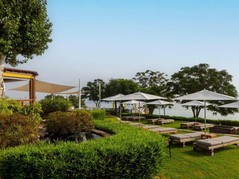 Grüne Gartenanlage mit Liegen, weißen Sonnenschirmen und Bäumen unter klarem Himmel.