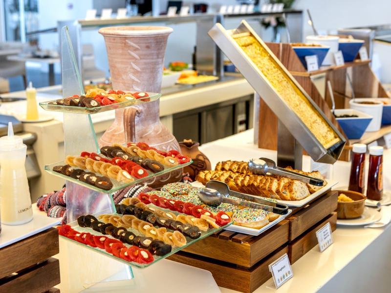 Buffet mit verschiedenen Brotsorten, Aufschnitt, Saucen und Getränken in heller Cafeteria.