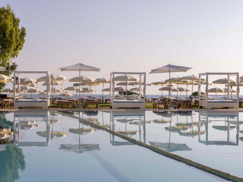 Schwimmbad mit Liegen und Sonnenschirmen, Spiegelung auf ruhigem Wasser bei klarem Himmel.