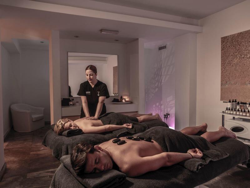 Zwei Personen liegen entspannt auf Massageliegen, während eine Therapeutin eine Massage gibt.