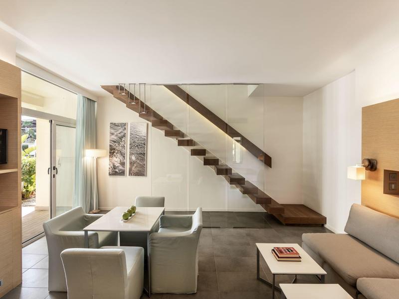 Moderner Wohnraum mit grauem Sofa, Sesseln, Holztreppe und großem Fenster für viel Tageslicht.