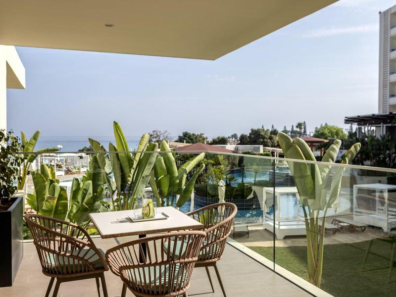 Moderner Balkon mit Glasgeländer, Tisch, vier Stühlen und Pflanzen, Blick auf Pool und Meer.