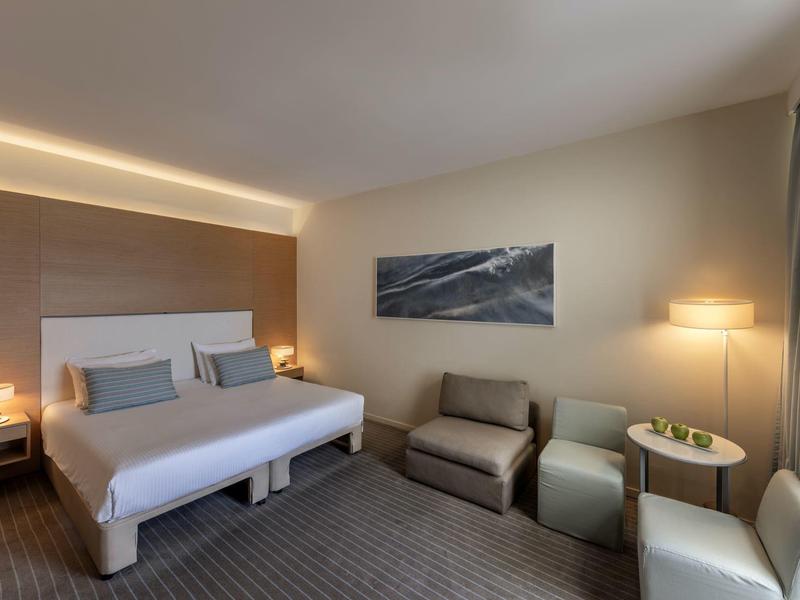 Modernes Schlafzimmer mit Doppelbett, Sitzgruppe, Teppichboden und sanfter Beleuchtung.