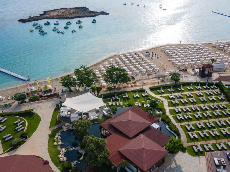 Widok z lotu ptaka na ośrodek nadmorski z leżakami, basenami i widokiem na morze.
