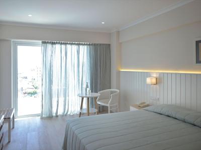 Světý hotelový pokoj s manželskou postelí, malým stolkem, židlí a terasou s výhledem ven.