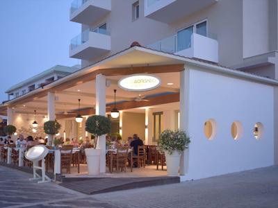 Open restaurant met moderne witte stoelen en gedekte tafels naast een hotel.