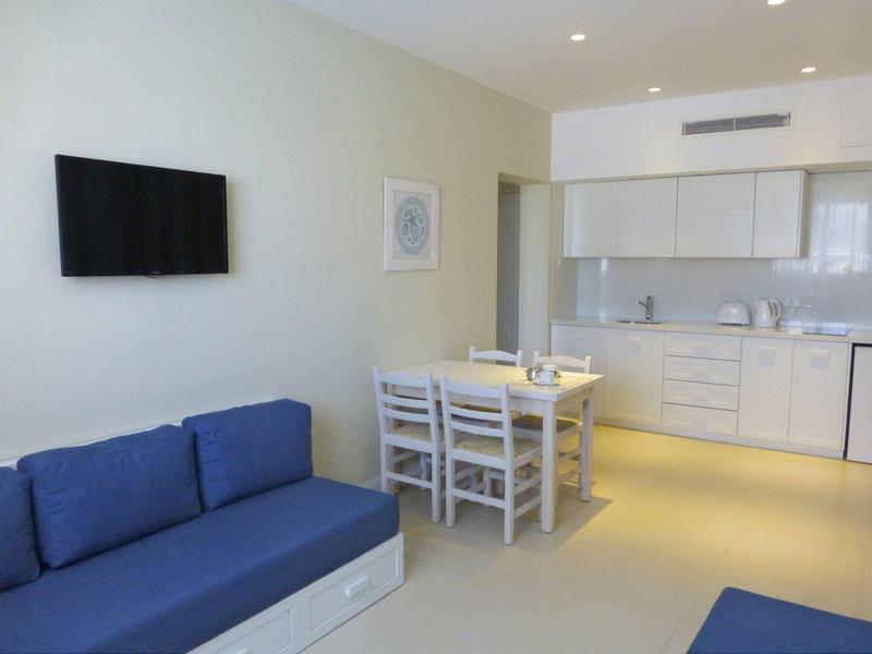 Moderne hotelkamerinrichting met blauwe bank, eettafel en kitchenette.