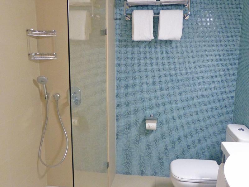 Moderne hotelbadkamer met douche, toilet, handdoeken en wastafel op witte tegelvloer.