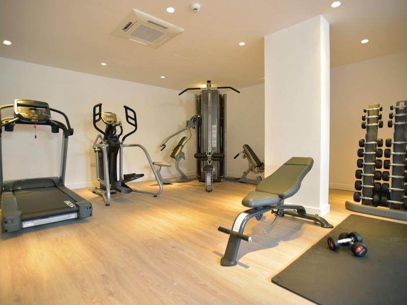 Lichte sportschool met loopband, crosstrainer, gewichtbank en halters.