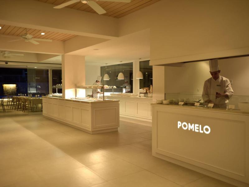 Heler restaurantinterieur met kok achter de balie en zitgedeelte op de achtergrond bij avondlicht.