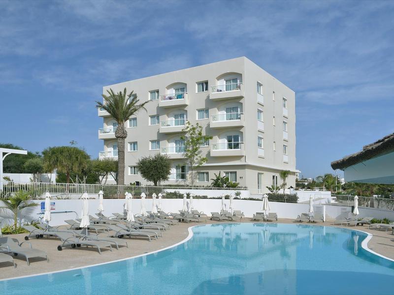 Modern hotelgebouw met zwembad en ligstoelen onder blauwe lucht