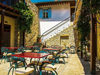 Hof mit roten Tischen, grünen Stühlen, Steintreppe und Weinreben an den Wänden bei Sonnenschein.