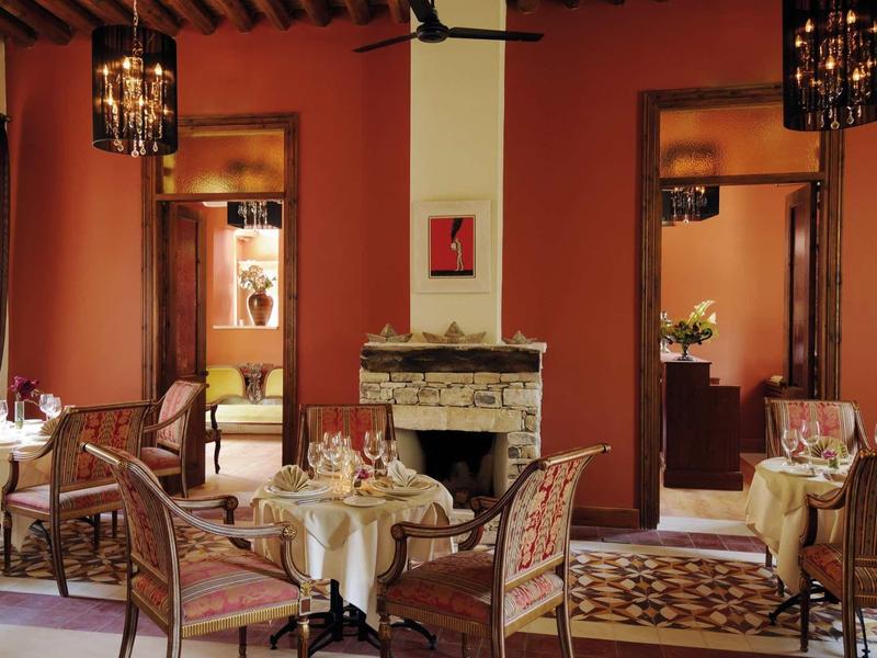 Elegantes Restaurant mit rot-orange Wänden, Kamin, runden Tischen und kunstvollen Kronleuchtern.