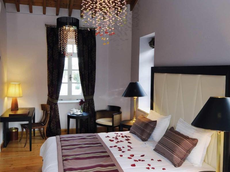 Elegantes Schlafzimmer mit Holzbalkendecke, Kronleuchter, Doppelbett und dunklen Möbeln.