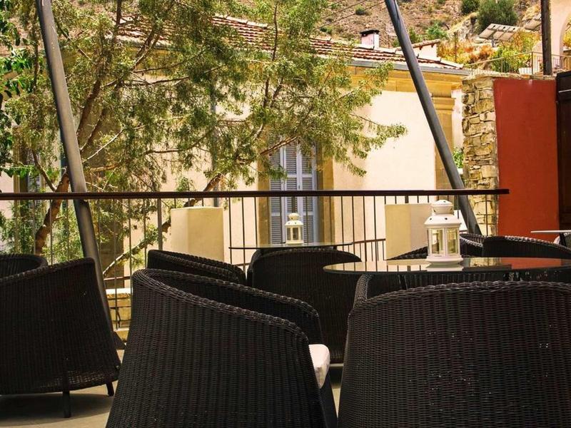 Terrassenbereich mit schwarzen Korbstühlen und Tischen, umgeben von Metallgeländer und Bäumen.