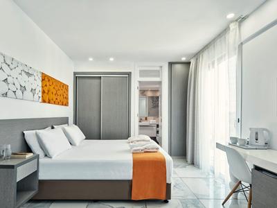 Helles Schlafzimmer mit Doppelbett, grauem Kopfteil, orangenem Deckenstück und großem Fenster mit Vorhängen.