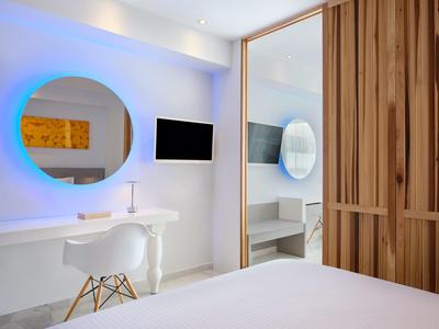 Nowoczesny pokój hotelowy z białym biurkiem, krzesłem i podświetlanym lustrem na ścianie.