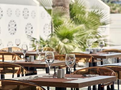 Pusty teren zewnętrzny restauracji z nakrytymi stołami i palmami w tle.