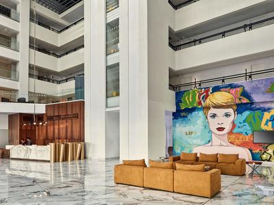 Nowoczesna lobby hotelowa z marmurową podłogą, skórzanymi sofami i kolorową sztuką na ścianie.