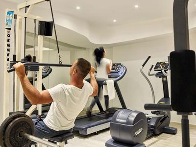 Dwie osoby ćwiczą w nowoczesnej siłowni z bieżnią i sprzętem siłowym.