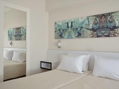 Nowoczesny pokój hotelowy z dużym łóżkiem, białymi poduszkami i abstrakcyjną sztuką na ścianie.