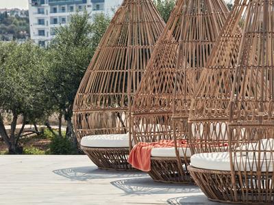 Drei geflochtene Rattansitze mit weißen Kissen und einem orangefarbenen Handtuch auf einer Terrasse.