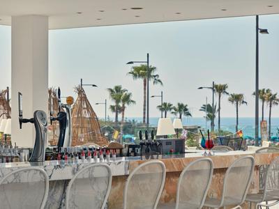 Offene Strandbar mit Metallstühlen, hölzernen Segelschiffen und Palmen am blauen Meer.