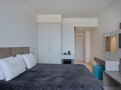 Modernes, helles Schlafzimmer mit großem Bett, weißen Wänden, Schrank und kleinem Sitzbereich.