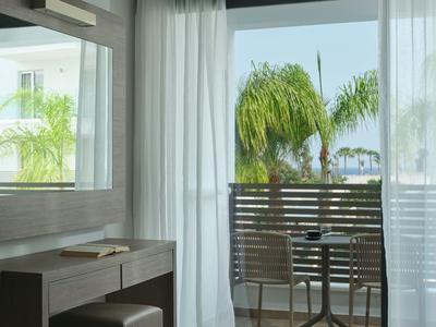 Jasny pokój hotelowy z meblami balkonowymi i widokiem na zielone palmy w świetle dziennym.