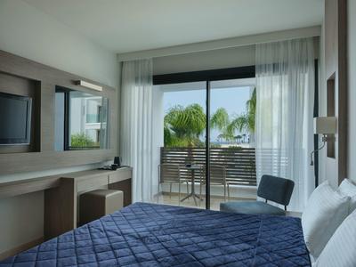 Modernes Schlafzimmer mit blauem Bett, Schreibtisch, Stuhl und Balkon mit Palmenblick.