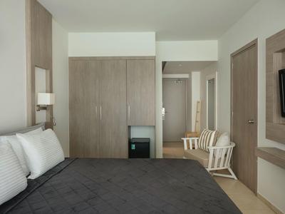 Nowoczesny pokój hotelowy z dużym łóżkiem, drewnianymi szafami i dwoma białymi krzesłami przy ścianie.