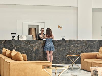 Moderne Rezeption mit schwarzer Marmorfront, beiger Sitzgruppe und Frau im blauen Kleid.