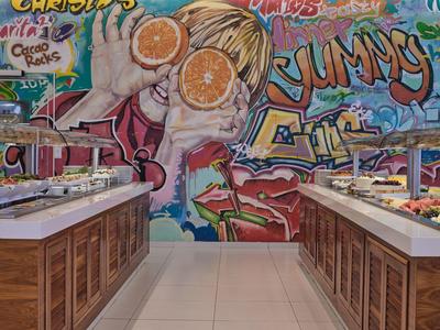 Buffet mit verschiedenen Speisen vor farbenfrohem Graffiti mit Orangen und Schriftzügen.