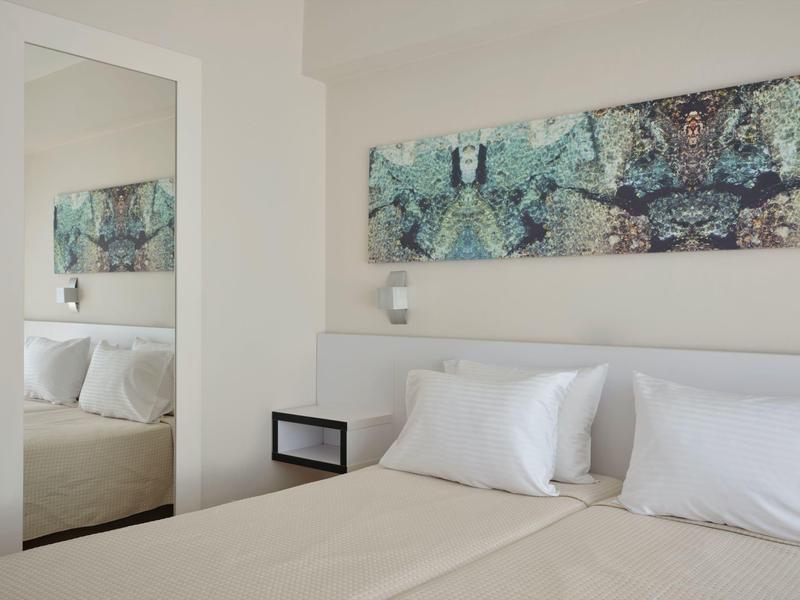 Hell eingerichtetes Schlafzimmer mit weißem Bett, Kissen, modernem Wandbild und großem Spiegel.